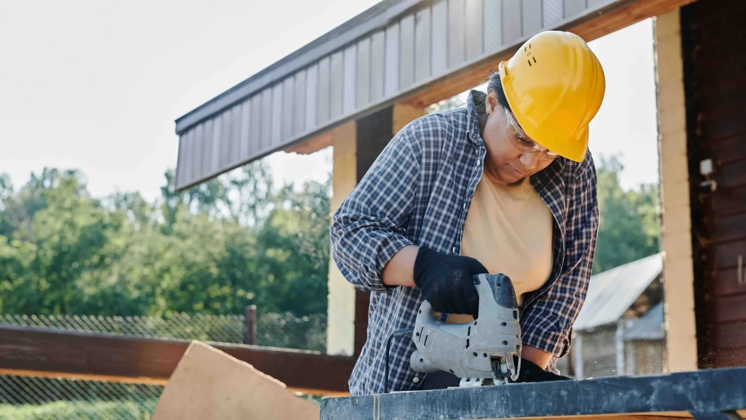 Ratenkauf - Frau mit gelbem Helm schneidet Holz mit Säge