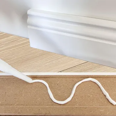 Weiße Sockelleiste wird verklebt montiert.