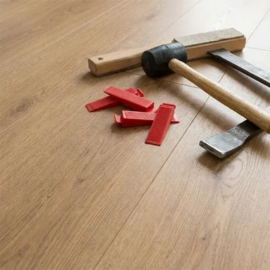 Ein heller Laminatboden von HORI, auf dem ein Hammer und weiteres Zubehör liegt.